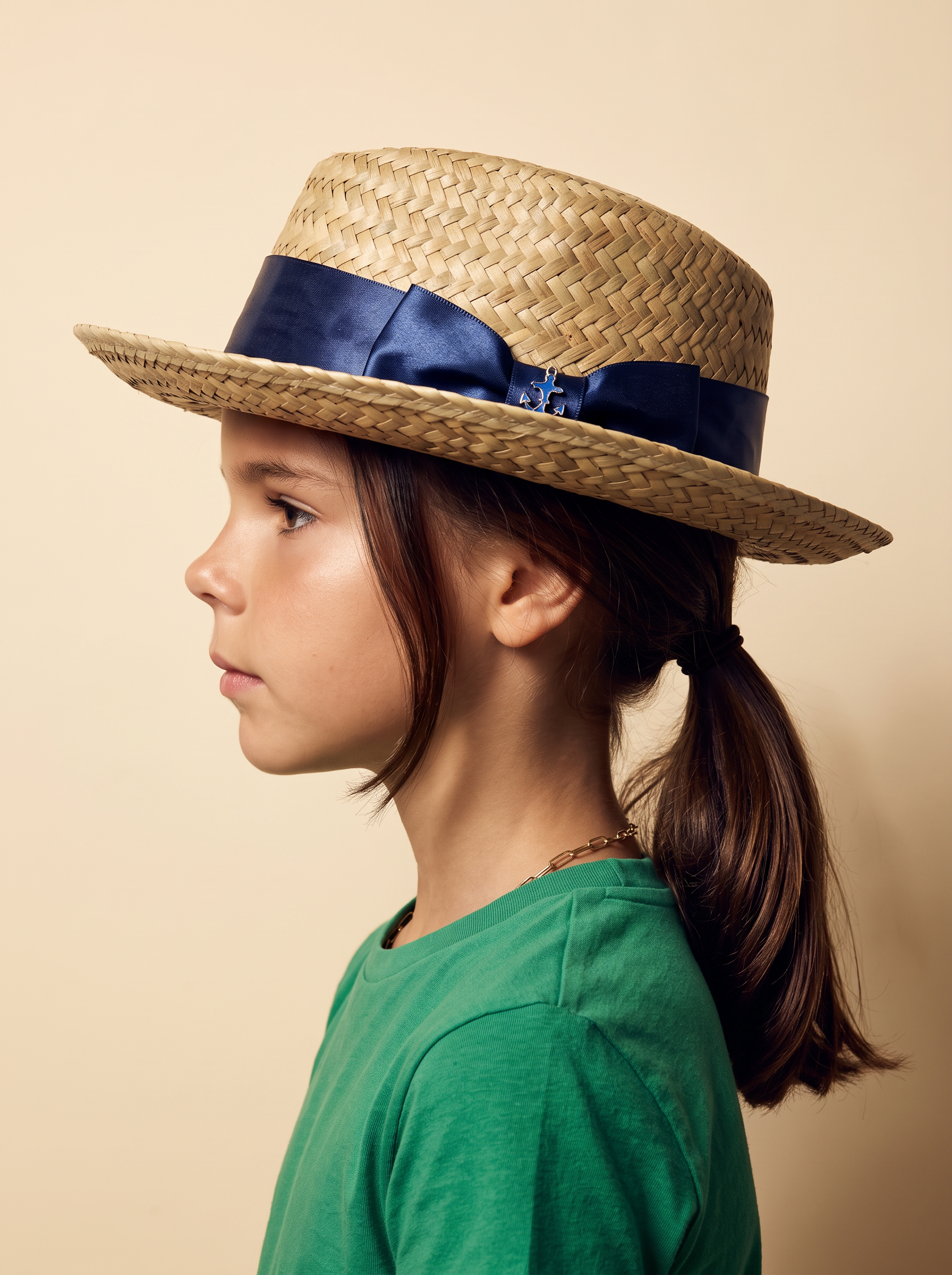 Profile portrait of a girl wearing a straw boater with a navy satin bow and blue charm