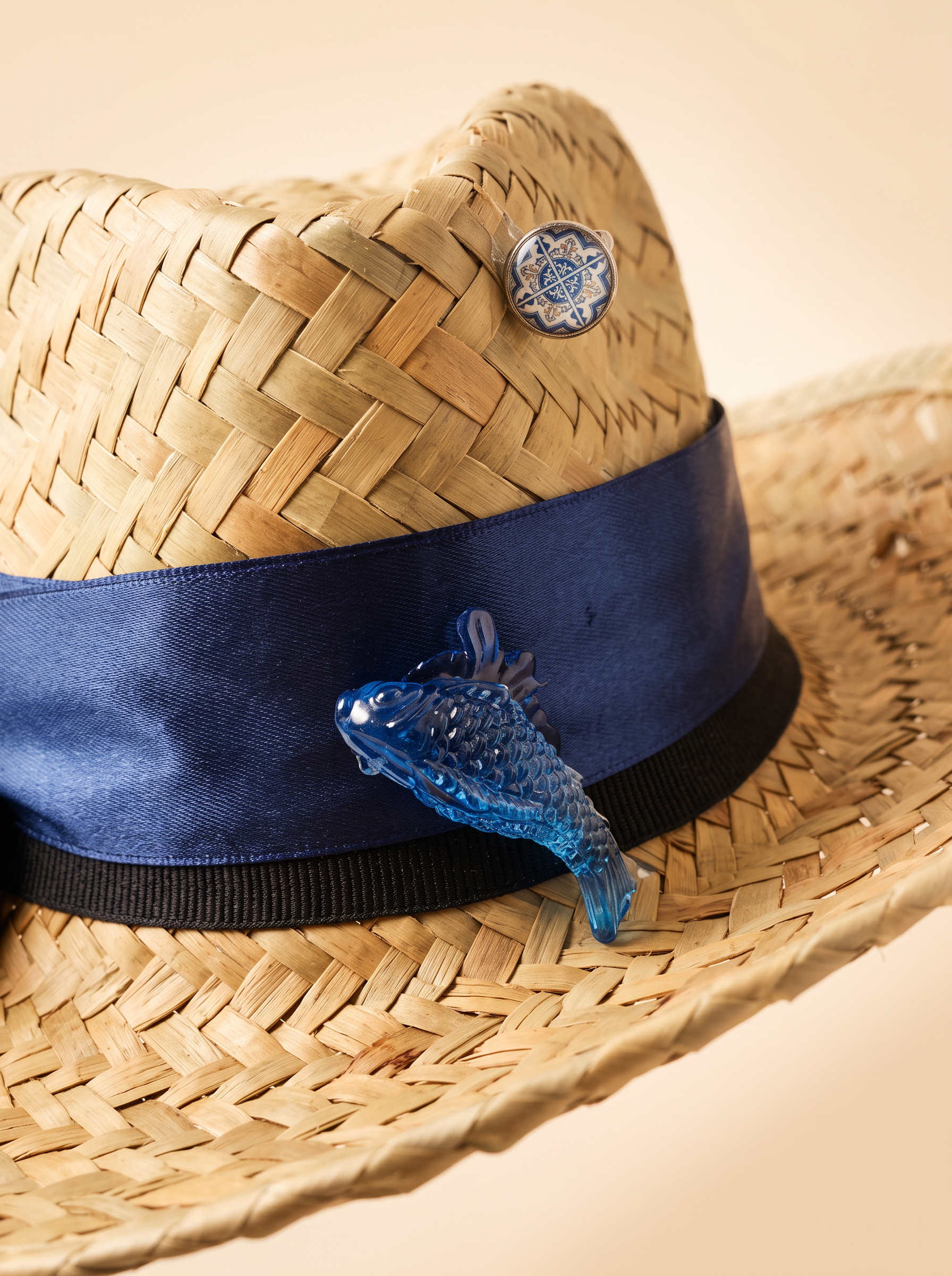 Macro detail of a finished straw hat brim with navy band and blue glass fish charm