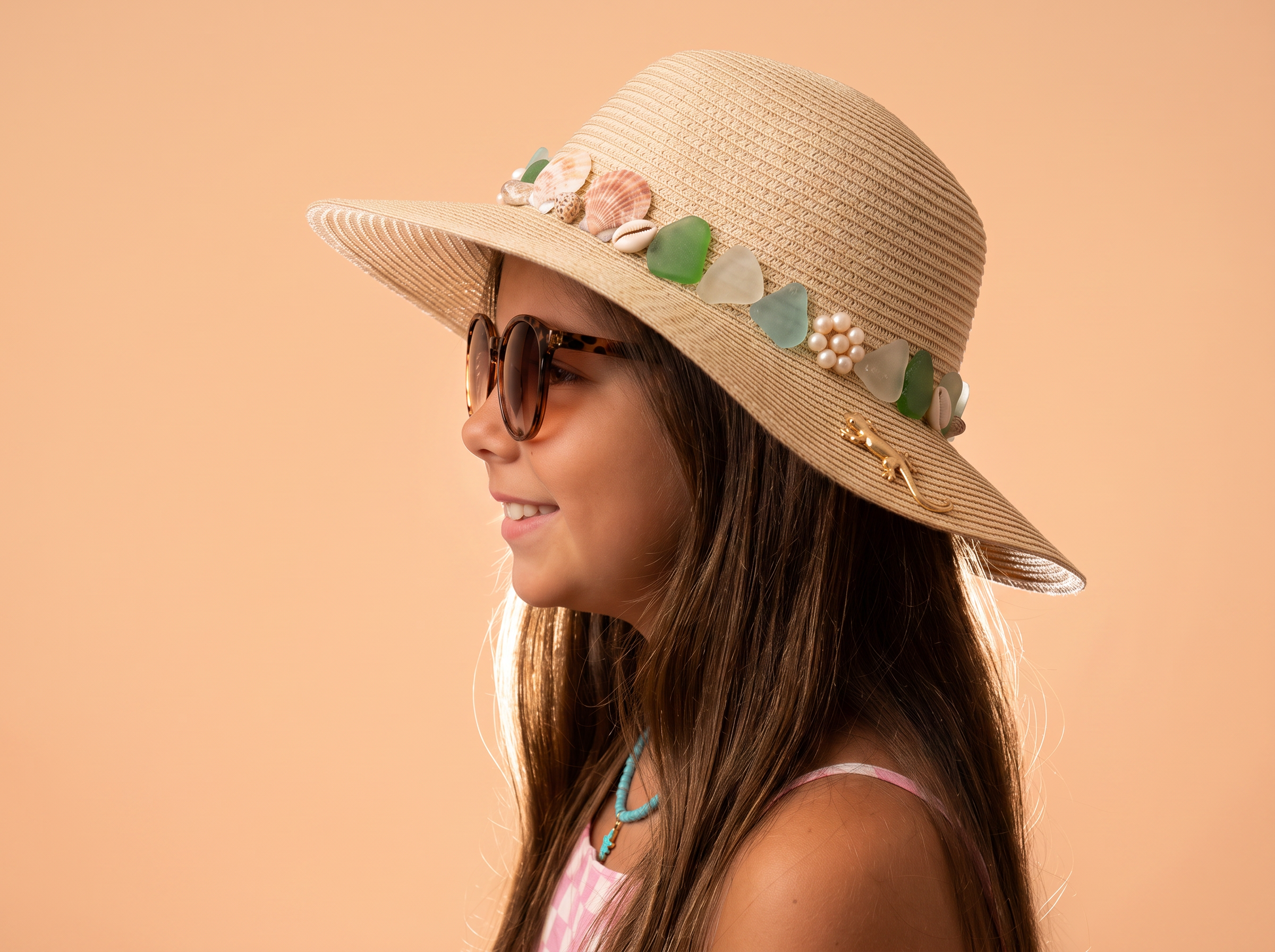 Profile of Francesca in sunglasses wearing the Shell Song hat trimmed with shells, sea glass, a pearl cluster and a tiny gold gecko