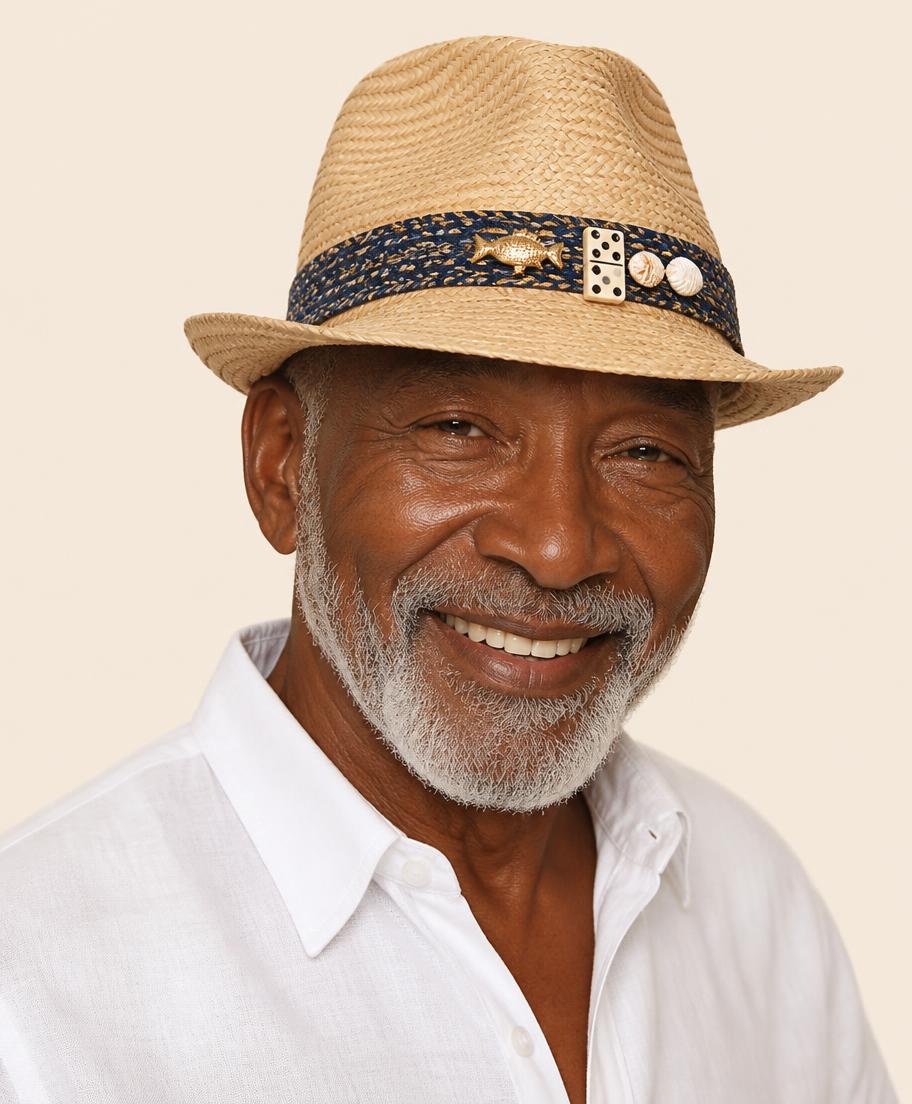 Caribbean man in his sixties with a grey beard and white linen shirt wearing a straw fedora with navy band, gold fish charm, domino and shells
