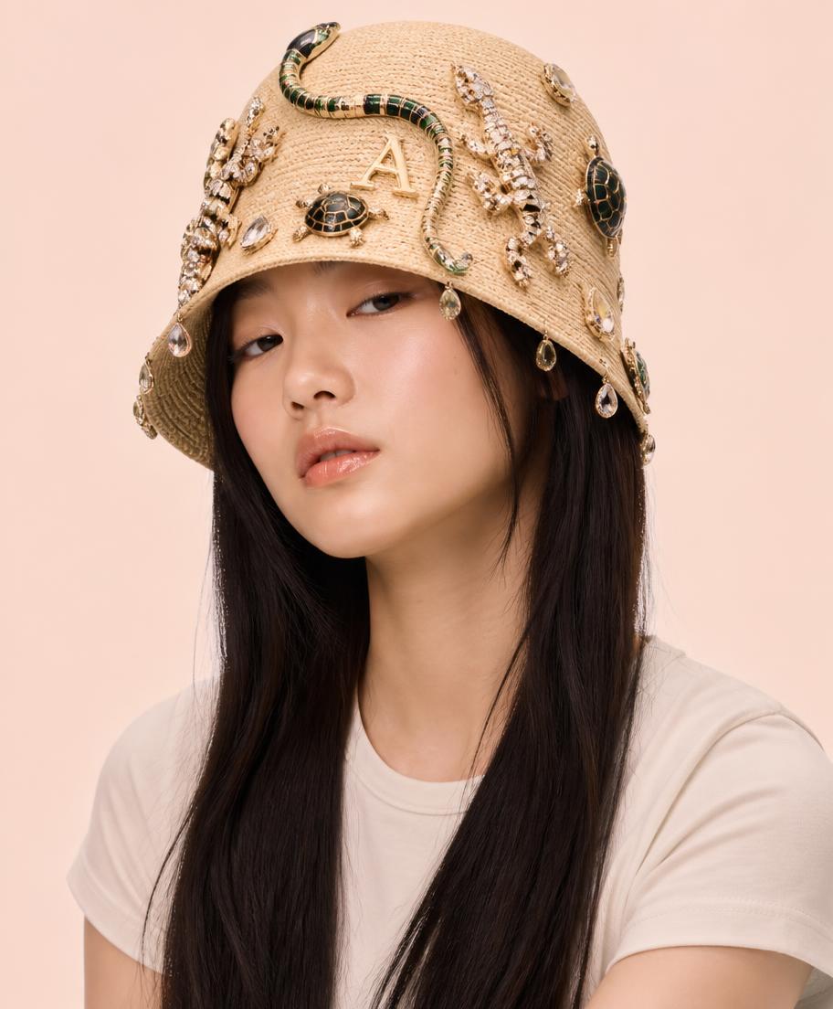 Korean teenager in a cream tee wearing a straw bucket hat covered in jewelled geckos, a beaded snake, enamel tortoises and crystal drops